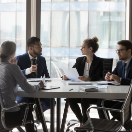 Four people in a business meeting at a table with paperwork, books and computer. 